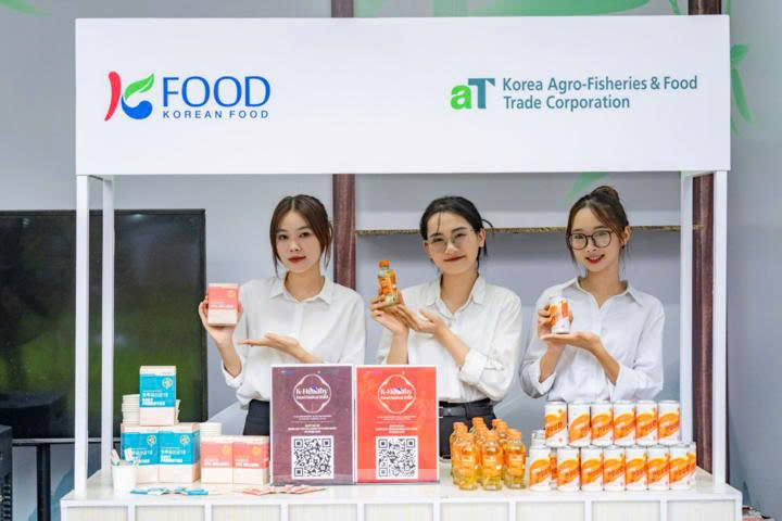 A group of women standing in front of a table with food productsDescription automatically generated